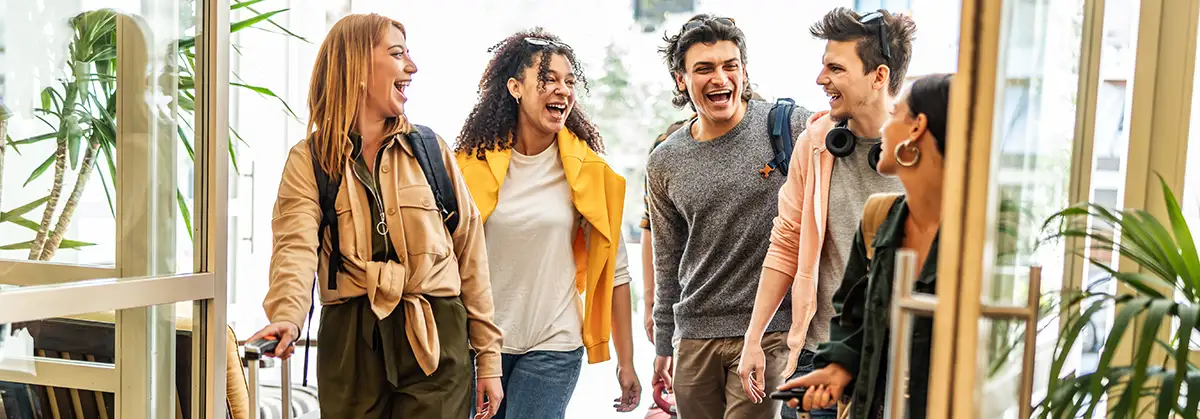 Eine Gruppe junger Touristen mit Koffern kommt in einer Jugendherberge an – Fröhliche Freunde genießen gemeinsam ihre Sommerferien – Millennials checken in der Hotellobby ein – Sommerferien